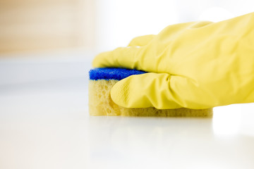 Female hand in rubber yellow glove cleans surface of table