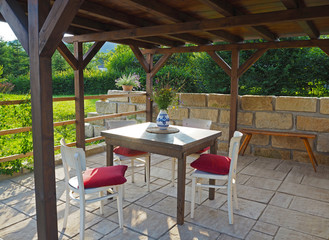 brown tiber wooden gazebo - pergola with table and chairs with red pillows with sandstone wall and...