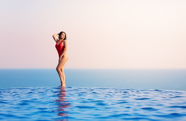 Woman Model posing In Infinity Swimming Pool. Ocean in background