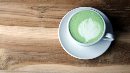 A cup of latte green tea with milk on a wood table. Aroma and flavor Japanese green tea beverage. Latte art created by pouring steamed milk.