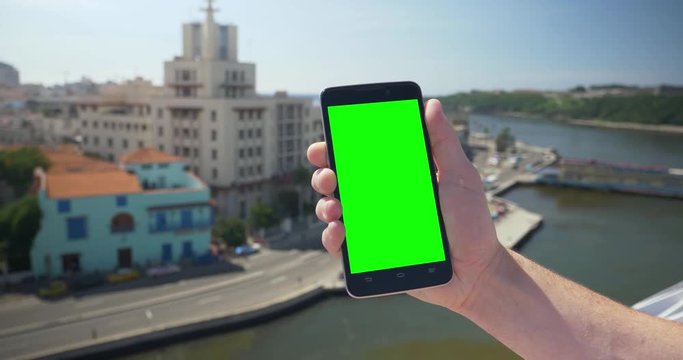Holding a green screen smartphone in portrait mode high above the Havana, Cuba shoreline. With optional corner markers for advanced tracking.  	