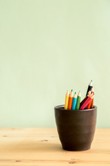 Fototapeta premium Color pencils in brown ceramic cup on wooden table