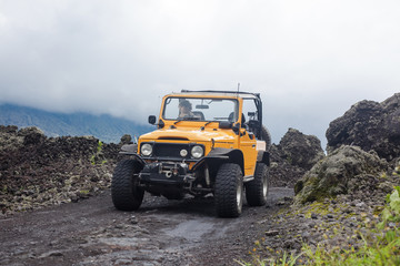 A curly-haired man is looking away driving an offroad yelow vehicle at the top of a valley with...