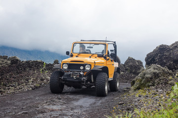 A curly-haired man is looking away driving an offroad yelow vehicle at the top of a valley with dark ground road © Dana Keli