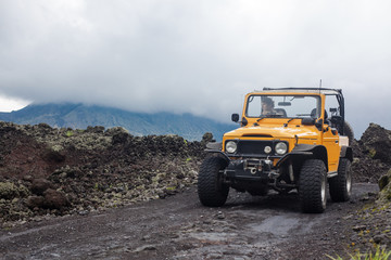 A curly-haired man is looking away driving an offroad yelow vehicle at the top of a valley with dark ground road © Dana Keli