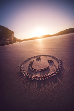 Smiling face drawn on a sandy beach with sundown in the background.