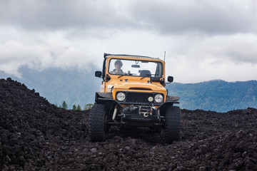 Frontside view of a curly-haired driver in yelow offroad vehicle parked at the top of a valley with volcanic rock and mountains in Bali, Indonesia © Dana Keli