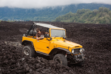 Fototapeta premium A curly-haired man in the offroad yelow vehicle got stuck at the top of a valley in volcanic rock. Bali, Indonesia