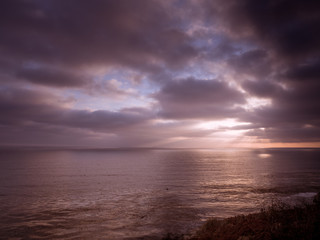 Fototapeta na wymiar Beams of sunlight show through a cloudy sky onto the ocean