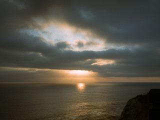 Obraz premium Beams of sunlight show through a cloudy sky onto the ocean