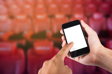 Smartphone on hand and white screen with blurry background of seat in movie theater.