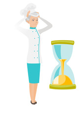 Worried senior caucasian chef looking at hourglass