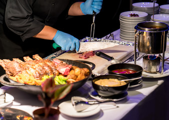 Hotel chef slicing grilled beef spare rib with long knife and fork