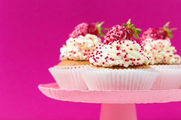 Vanilla cupcakes decorated strawberries on a pink cake stand with pink background