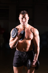 Fototapeta na wymiar Athletic shirtless young male fitness model holds the dumbbells.