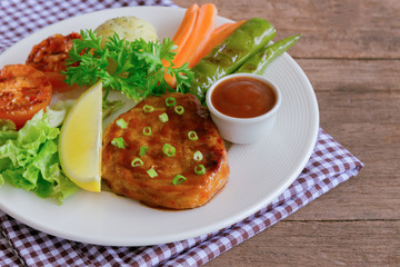 Barbecue pork steak on white plate served with barbecue sauce and vegetables. Pork steak for lunch or dinner on wood table. Moist and soft homemade pork barbecue served with mash potato and vegetable.