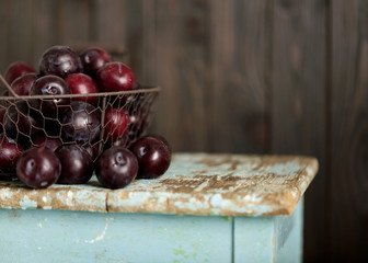 Ripe plums in a basket on a wooden background.