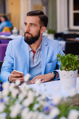 Stylish bearded male in a blue jacket using smartphone.