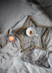 A cup of coffee and a candle in a Scandinavian wooden tray in a cozy bed 