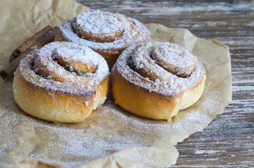 Fresh Delicious  cinnamon  rolls with powdered sugar, metal strainer and cinnamon stick on wooden table. Sweet food background.