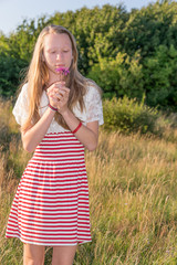 ein junges blondes Mädchen mit langen Haaren riecht an einer Blumen Blüte in der Abendsonne im...