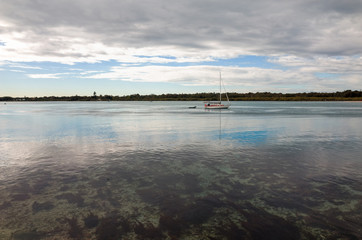 Sailboat cruising with furled sails on Australian lake