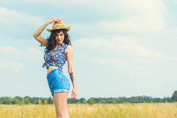 Beautiful hot sexy woman with bright make up wearing in american country style, straw hat and jeans shorts on a gold field background sky