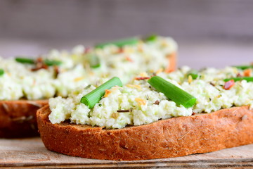 Avocado guacamole toast with spices and fresh green onions on a wooden board. Avocado guacamole on toast recipe. Closeup