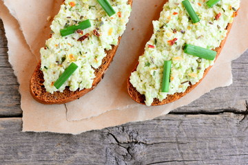 Guacamole toast sandwich with spices and fresh green onions on paper and a vintage wooden background. Guacamole toast sandwich recipe. Top view