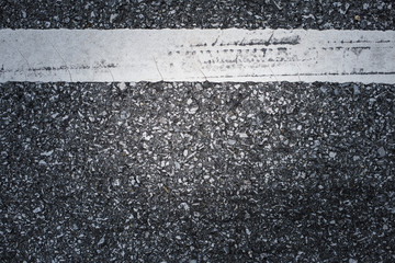 Fototapeta premium A dark asphalt pavement texture with aged and weathered horizontal traffic sign painted with white color