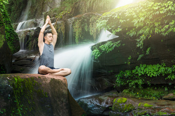 Young man meditating and relax in lotus position while doing yoga on the rock between waterfalls