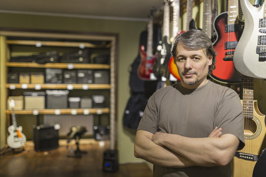 Portrait of confident male owner standing with arms crossed by guitars at store