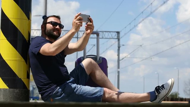 Handsome man sitting on the platform and doing selfies on smartphone
