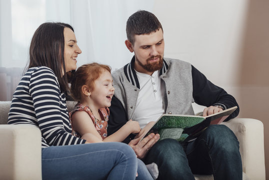 Parents reading book with daughter while sitting on sofa at home