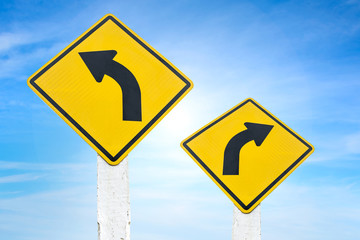 Yellow road signs indicating left and right turn with blue sky background.