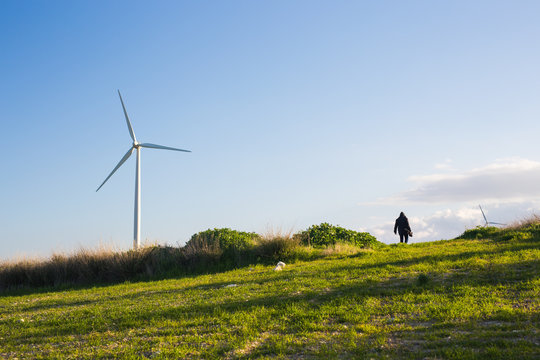 green meadow with Wind turbines generating electricity and man going into the distance