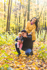 Fototapeta premium Happy young family in the autumn park outdoors on a sunny day. Mother, father and their little baby girl are walking in the park. Love and family concept.
