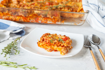 Traditional Italian lasagna baked with herbs and a piece of lasagna on a white plate.