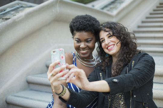 Happy woman taking selfie with young female friend against steps