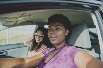 Young woman sitting with female friend looking away while sitting in car on sunny day