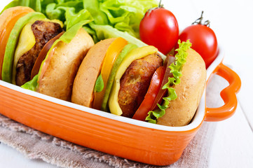Sandwiches (burgers) with yellow and black tomatoes, juicy cutlet, avocado on a white wooden background. Close up