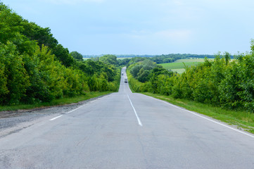 Asphalt road, goes into the distance. Green trees are on both sides.