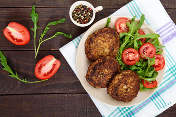 Juicy cutlets on a plate with a salad of tomatoes and arugula on a dark wooden background. Top view.