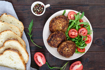 Juicy cutlets on a plate with a salad of tomatoes and arugula on a dark wooden background. Top view.