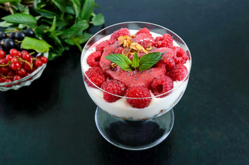 Delicious healthy dessert: yoghurt, fresh berries, granola, raspberry sauce on a black background.