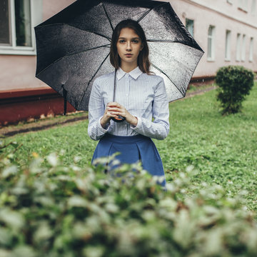 Portrait of teenager holding umbrella while standing on grassy field during rain