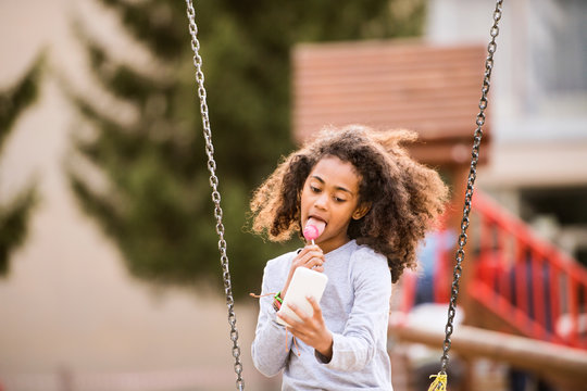 African American Girl On Swing With Smart Phone Texting.