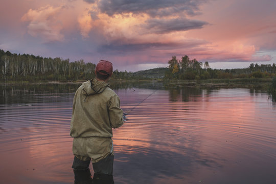 Rear view of man fishing in lake during sunset
