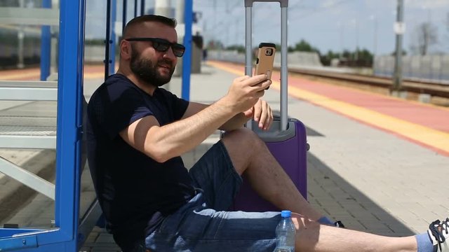 Man doing selfies on smartphone while sitting on the platform and waiting for the train
