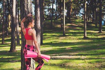 Young fit athletic woman wearing smart watch and holding yoga mat, ready for her workout in a forest. Mind and body happiness concept